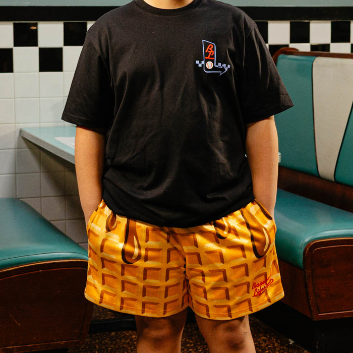 Person wearing a black t-shirt with BL101 logo and waffle shorts in a retro setting.