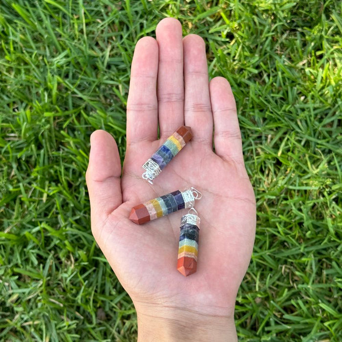 Three small cylindrical crystal bead charms with silver jump rings are resting on an open hand, set against a background of green grass.