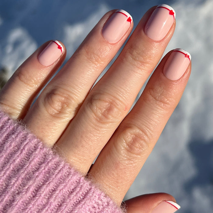 Classic French with CV Heart - Squoval | Extra Short nails with soft peach base and red heart tips on natural hand in sunlight