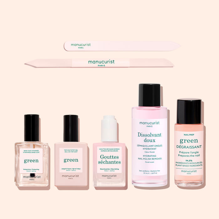 Six products from Manucurist’s "The Essentials of the Green™ System," including a nail file, gel effect manicure, plant-based nail polish, remover, drops, and degreaser, are arranged on a pale background. Each item showcases minimalist packaging in green and pink tones with Manucurist branding and highlights acetone-free formulas.