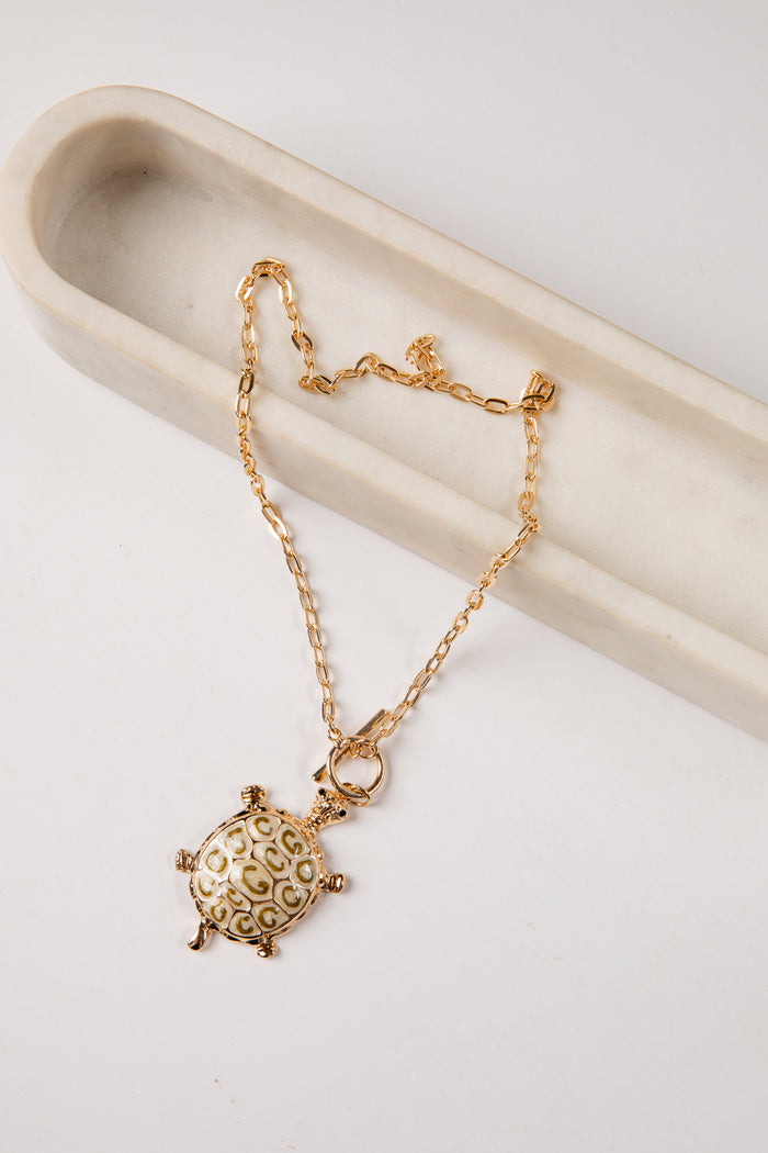 Gold necklace with a turtle pendant on a light background