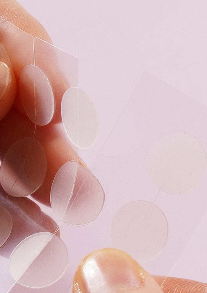 Close-up of clear adhesive patches on a finger against a light pink background