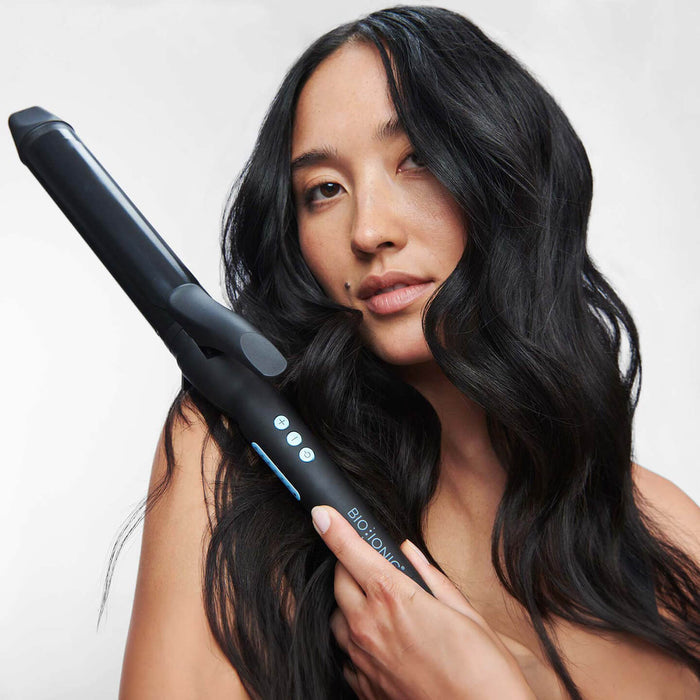Woman with long dark wavy hair holding long barrel curling iron.