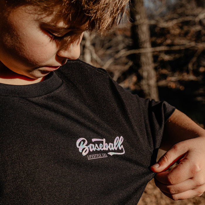 Person wearing a black t-shirt with 'Baseball Lifestyle 101' text, standing outdoors.