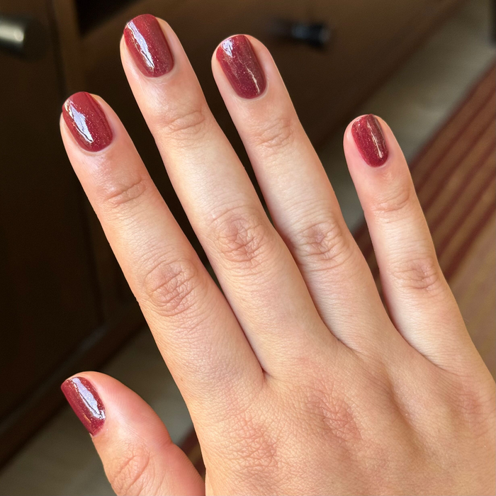 Saucy deep red quick dry gel polish shown on natural short nails with soft indoor lighting background