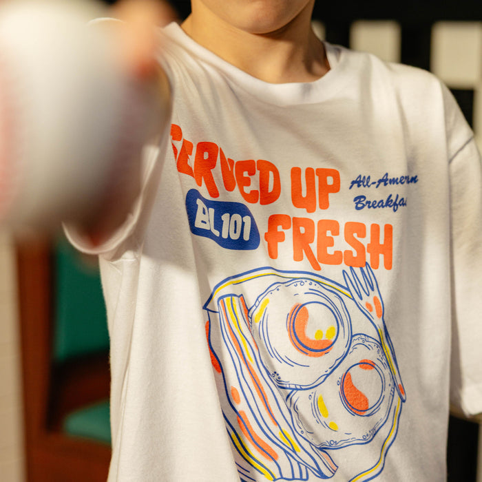 Close up of white t-shirt with a bacon and egg graphic and 'Served Up BL101 Fresh' text