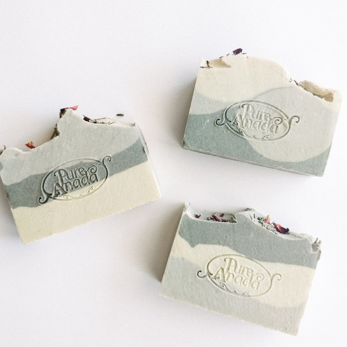Handmade natural bar soaps with a stamped logo, showing layers and ingredients within, placed on a light background.