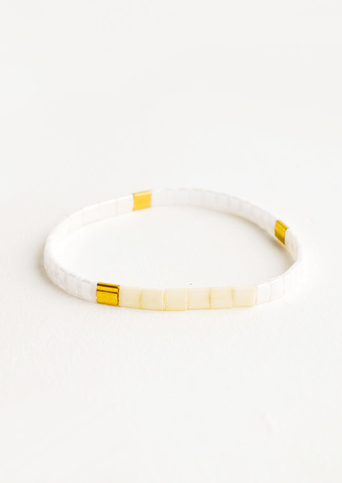 Bracelet featuring flat white beads interspersed with flat gold bead on an elastic cord.