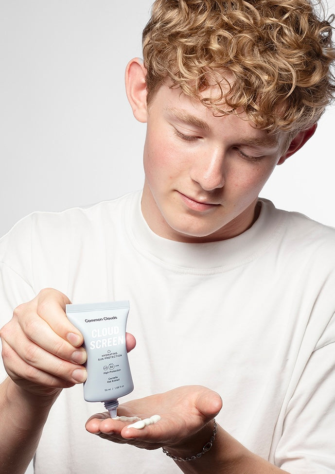 Person holding a skincare product and applying it to their hand against a white background
