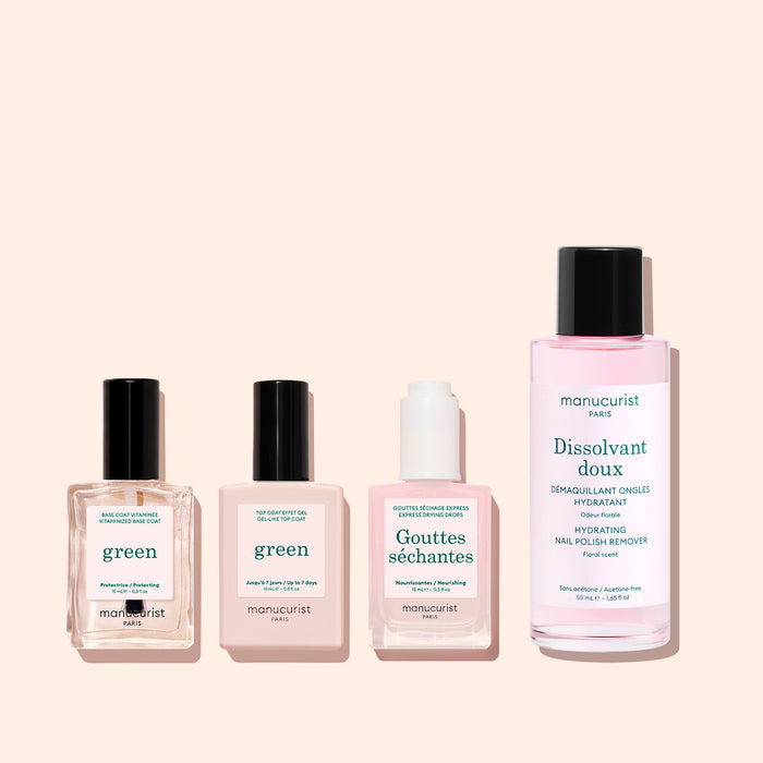 Four manicure products with pink and white labels stand side by side on a pale pink background, including nail polish, Manucurist's Vitaminized Base Coat Green™ formulated with KeraHCE+ technology to strengthen nails, nourishing nail care drops, and gentle nail polish remover.