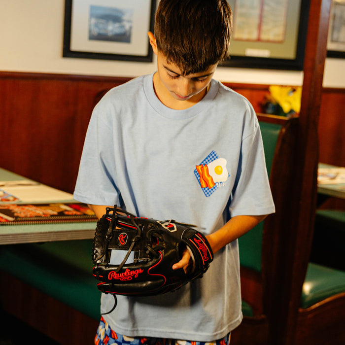 Child wearing a blue t-shirt with bacon and eggs on it while holding a baseball glove in a casual indoor setting