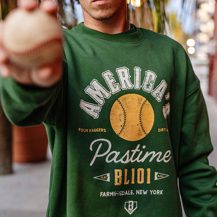 Close up of forest green America's Pastime crewneck sweatshirt graphic with a baseball held toward the camera