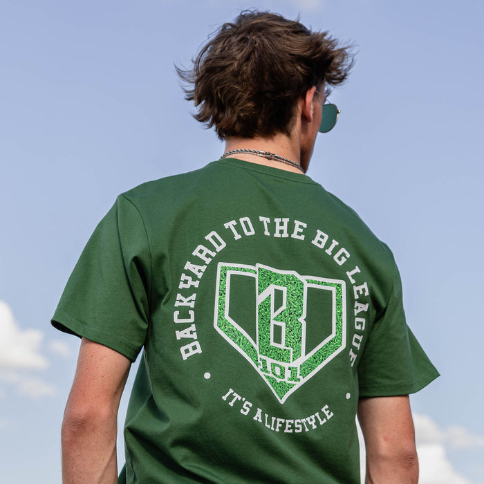 Back view of forest green tee with Backyard to the Big Leagues graphic featuring a grass textured home plate BL101 logo and It's A Lifestyle text