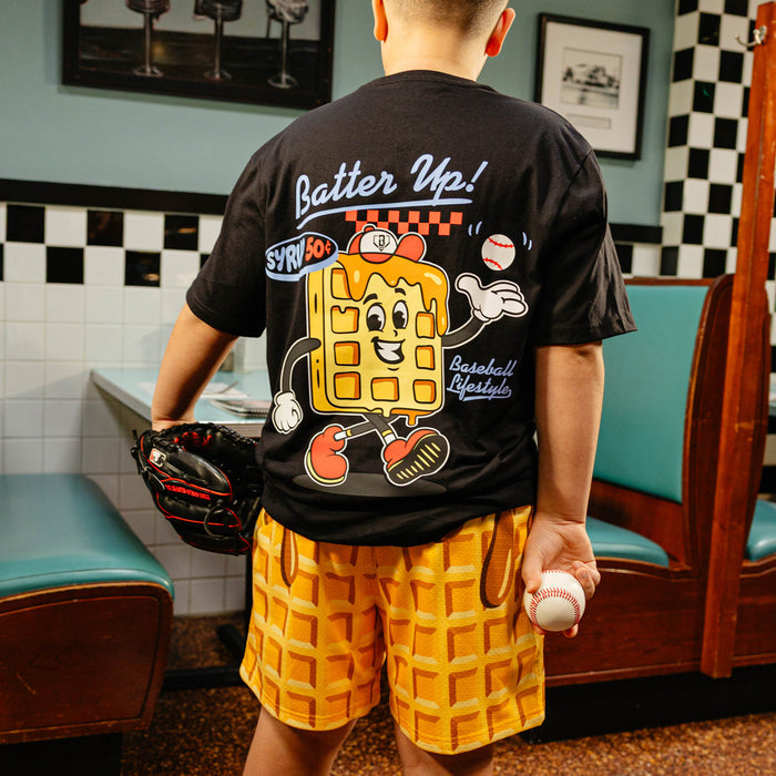 Person wearing a black t-shirt with a cartoon character and 'Batter Up!' text, holding a baseball in a retro diner setting.