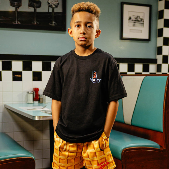 Young boy in a black t-shirt and waffle shorts standing in a diner.