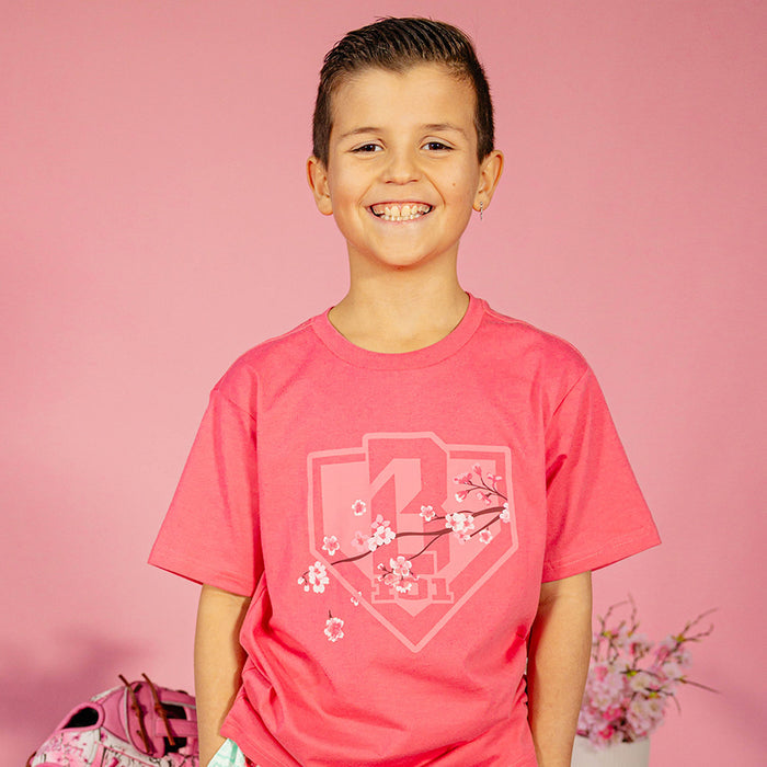 Young boy wearing a pink BL101 cherry blossom shield tee against a pink background, front view