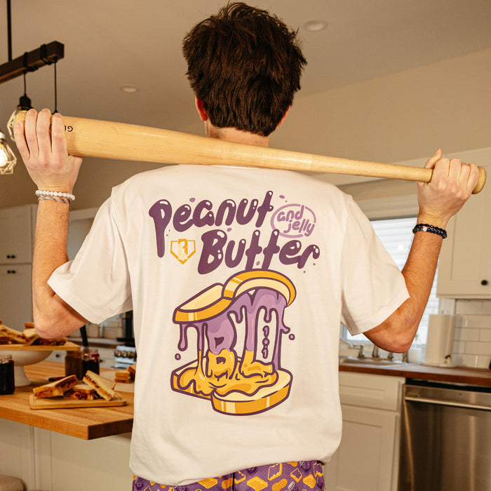 Back view of the BL101 Peanut Butter and Jelly white tee on a male model holding a baseball bat, showing the dripping sandwich graphic.