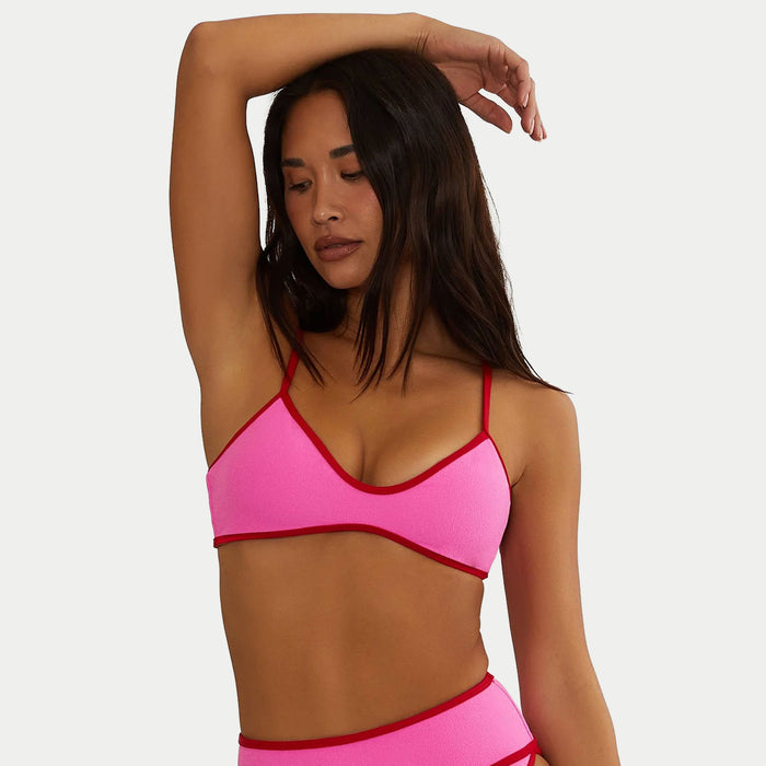 Woman wearing a pink bikini with red trim against a plain background