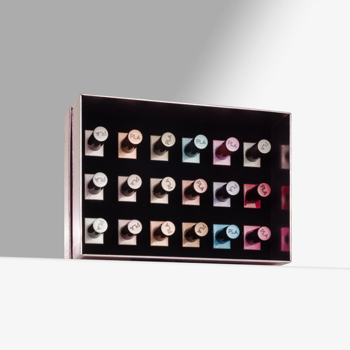 A rectangular pink box holding 18 nail polishes arranged in rows, photographed on a clean white surface against a light gray background.