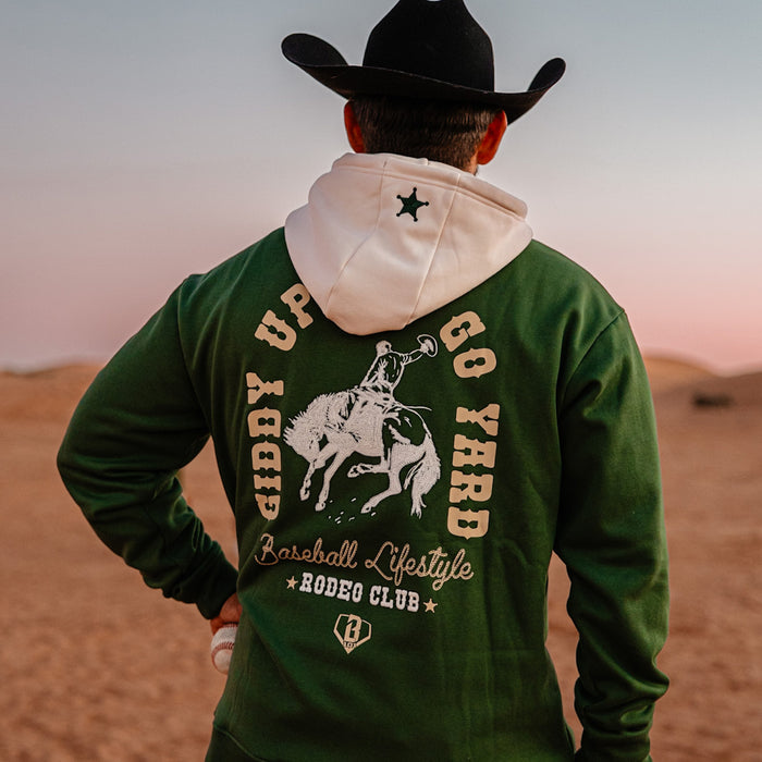 Person wearing a green hoodie with 'Giddy Up and Go Yard' text and horse graphics, standing in a desert landscape.