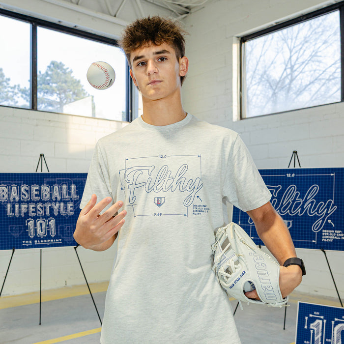 Person wearing a 'Filthy' t-shirt holding a baseball and glove indoors.