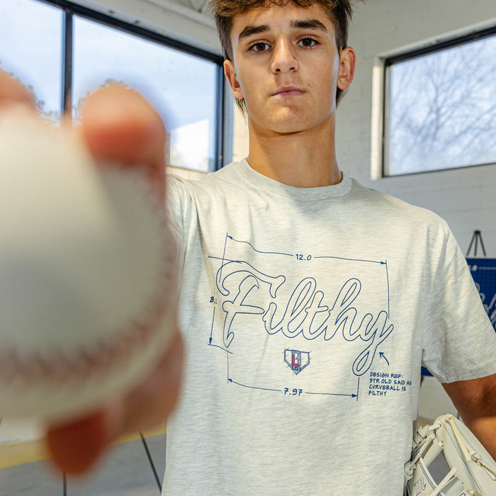 Person wearing a gray t-shirt with text 'Filthy' text, holding a baseball.