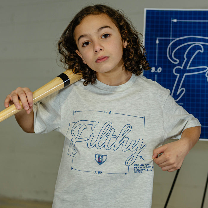 Child wearing a gray t-shirt with 'Filthy' design, holding a baseball bat indoors.