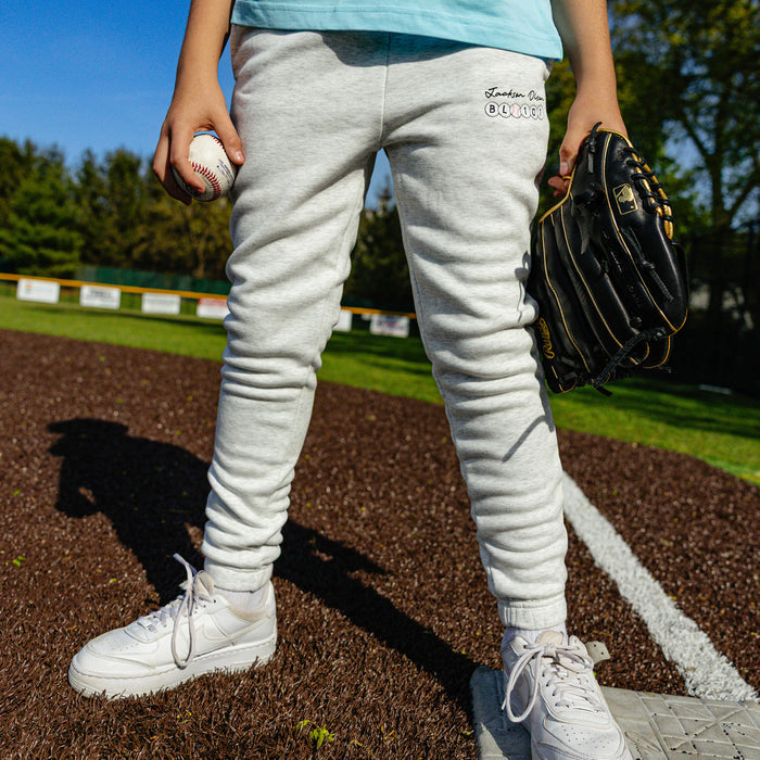 Close-up of the youth heather gray BSBL Era sweatpants showing the "Jackson Olson" script and BL101 baseball bead logo on the thigh