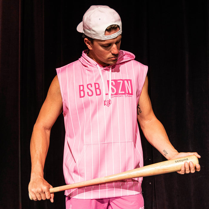 Adult male model holding a wood bat wearing the pink pinstripe Jackson Olson x BL101 BSBL-SZN Short Sleeve Hoodie V3 with matching pink shorts