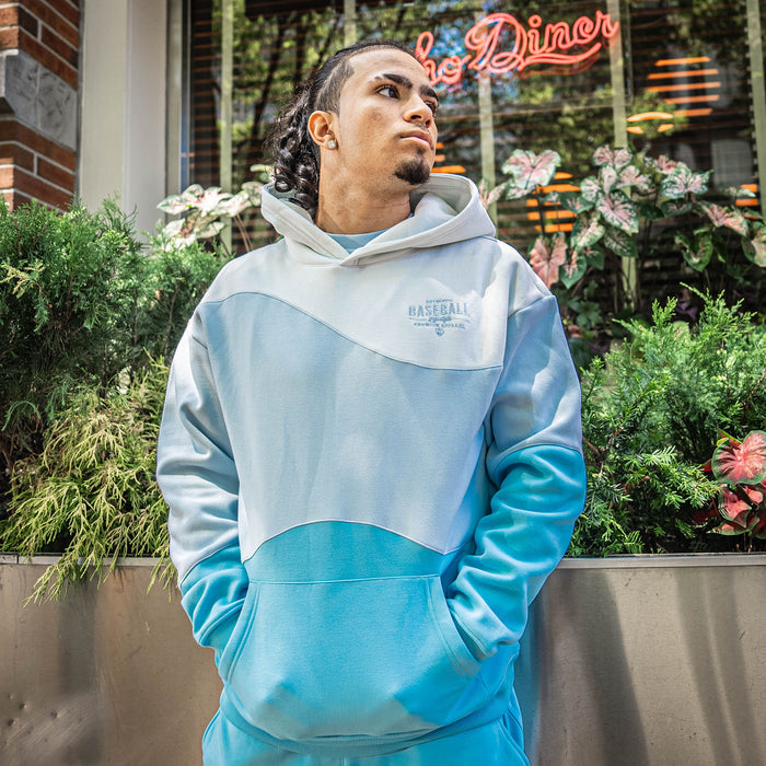 Person wearing a light blue hoodie with 'Authentic Baseball Lifestyle PREMIUM APPAREL' text, standing in front of a building with neon signs