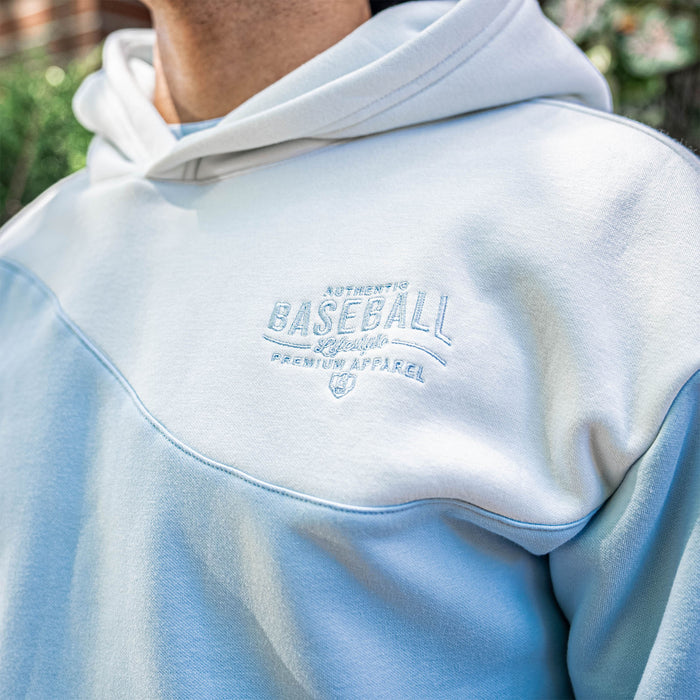 Light blue hoodie with 'Authentic Baseball Lifestyle PREMIUM APPAREL' text on a blurred background