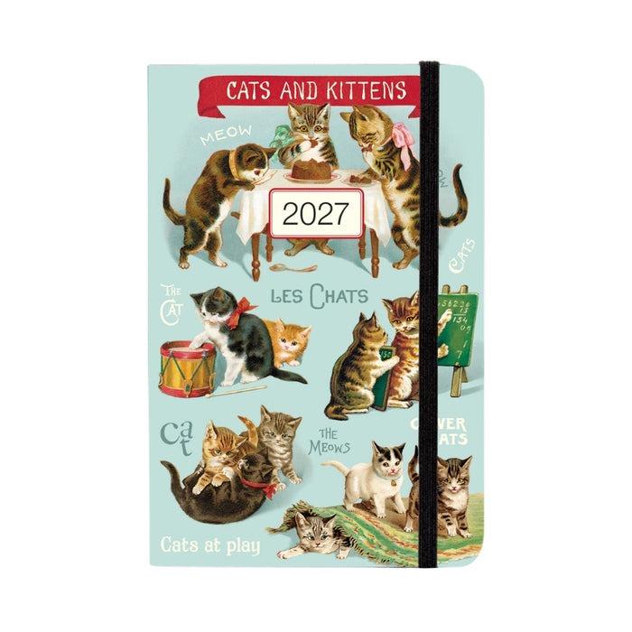A 2027 hardcover planner with a light blue cover decorated with vintage-style illustrations of various cats and kittens. The cover features a red banner at the top reading 'CATS AND KITTENS', a white label in the center reading '2027', and a black elastic closure band.