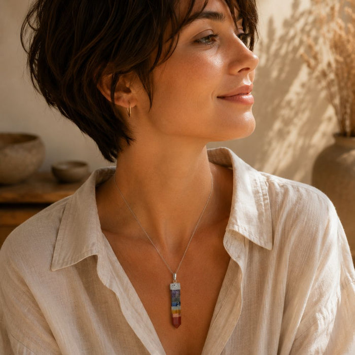 Person wearing a Chakra point pendant on a delicate silver chain with neutral clothing in warm natural light.