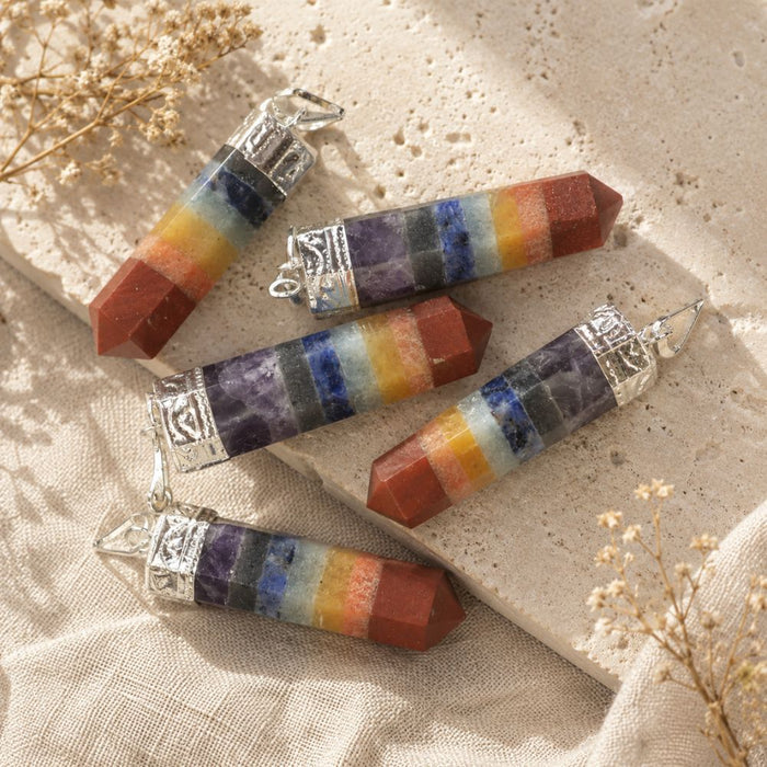 Chakra point pendants displayed on a natural stone surface with soft linen and dried botanicals.