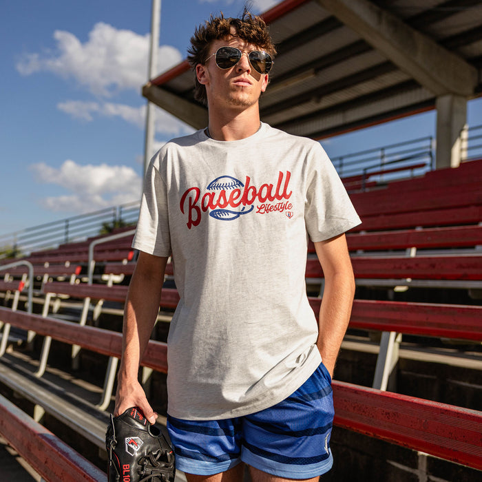 Male model wearing the BL101 Baseball Lifestyle heather gray tee and blue stripe mesh shorts at a stadium, holding a baseball glove.
