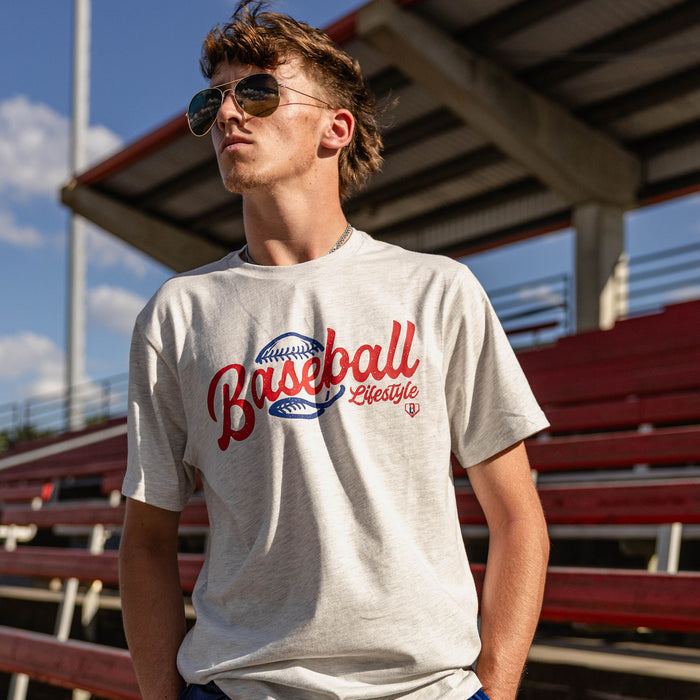 Male model wearing the BL101 Baseball Lifestyle heather gray tee at a stadium with bleachers in the background.