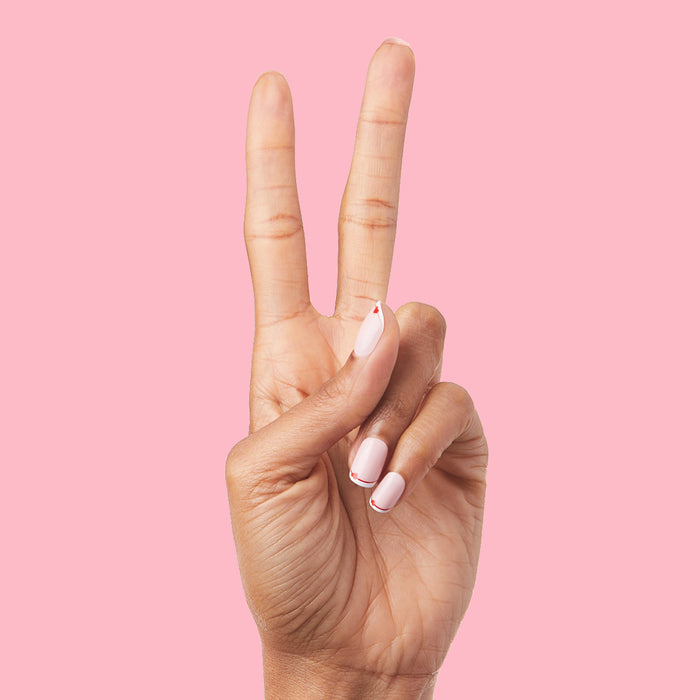 Classic French with CV Heart - Squoval | Extra Short with peachy pink base, white tips, and delicate red heart detail on hand against pink background