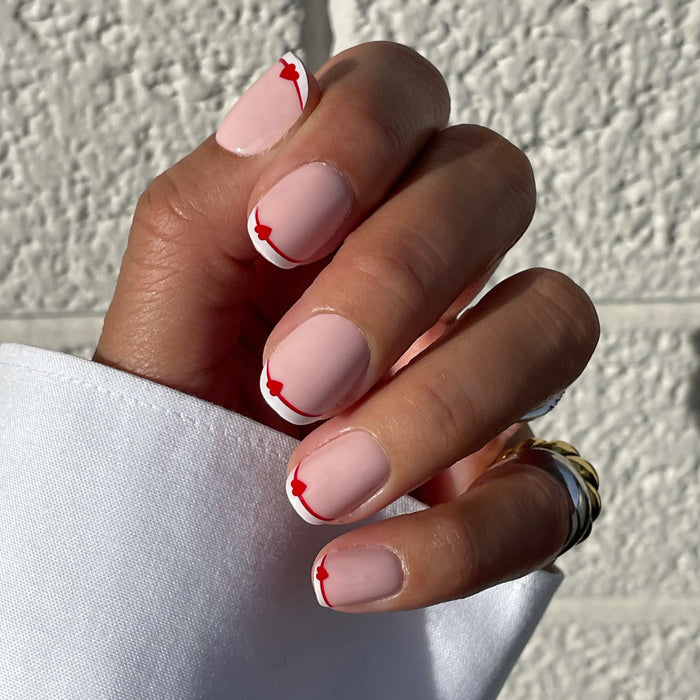 Classic French with CV Heart - Squoval | Extra Short with peachy pink base, white tips, and red heart accents on natural nails in sunlight