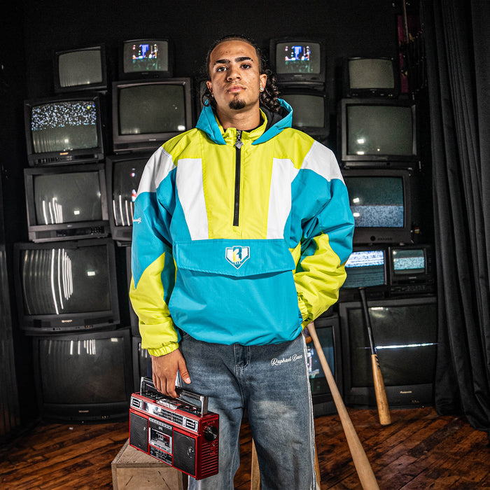 Person wearing a blue and yellow pullover jacket holding a boombox in front of stacked vintage TVs.