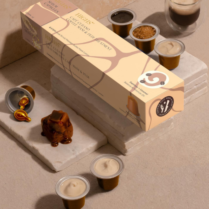 A boxed manicure and pedicure treatment set with various capsules and a chocolate-covered treat, displayed on a marble surface with cups of a liquid treatment.