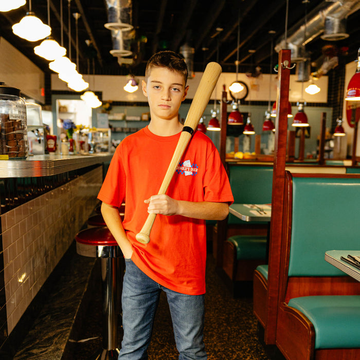 Person in a red shirt holding a baseball bat in a diner setting