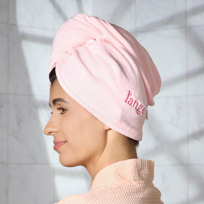 Woman wearing a blush pink L'ange microfiber hair wrap towel, profile view, in a robe