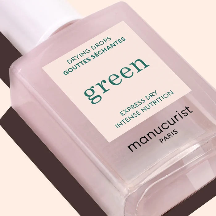 A close-up of Manucurist Drying Drops, labeled in English and French, promising express dry and intense nutrition for nourished cuticles, shown on a light beige background.