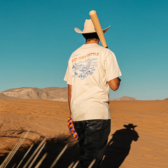 Adult model wearing white graphic tee with “Dust Don't Settle Relaxed” design