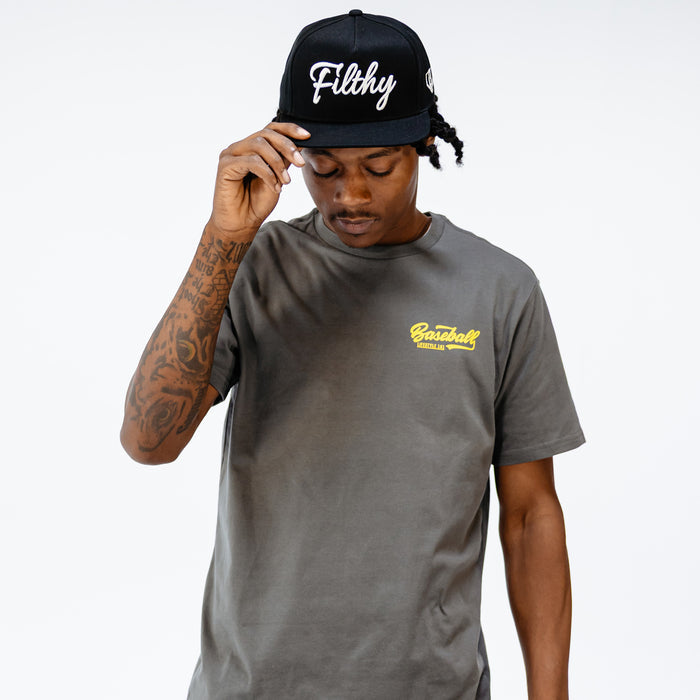 Person wearing a black cap with 'Filthy' text and a gray t-shirt with yellow 'Baseball Lifestyle 101' text in top corner