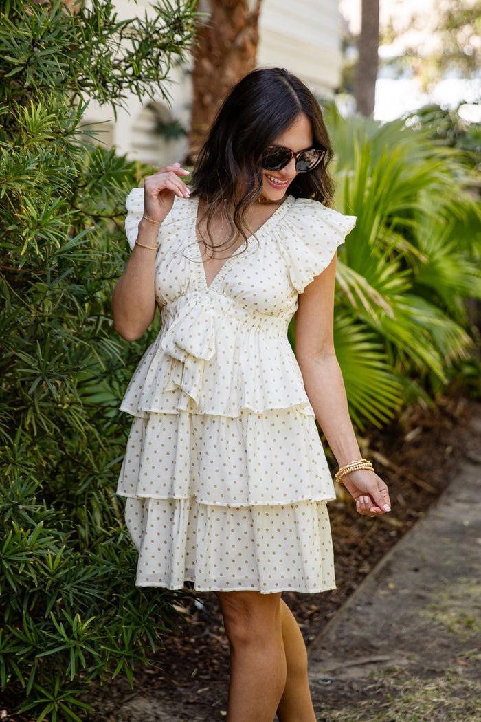 Woman wearing a white polka dot dress standing outdoors with greenery in the background