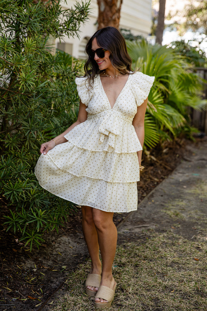 Woman in a white floral dress standing outdoors with greenery around