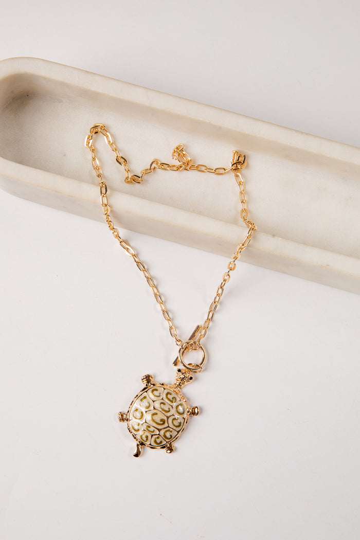 Gold turtle pendant necklace on a white surface