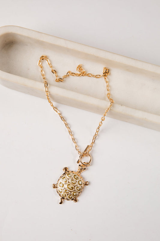 Gold turtle pendant necklace on a white surface