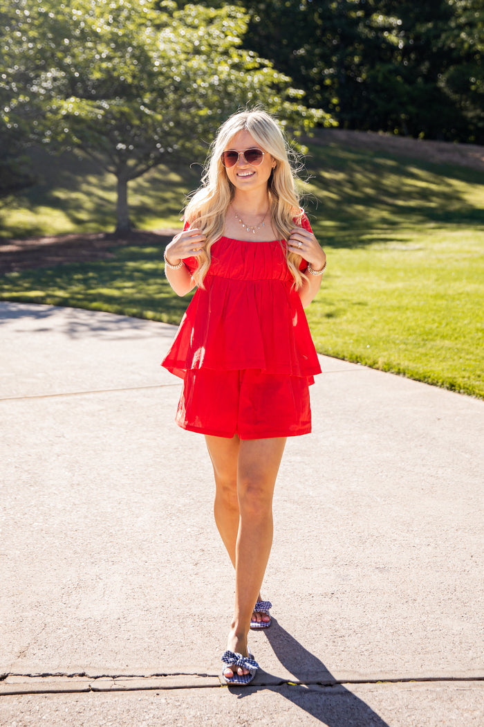 Woman in a red dress standing on a sidewalk with greenery in the background